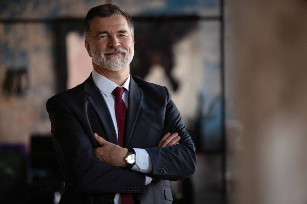 Confident CEO with arms crossed smiling while standing in his office.